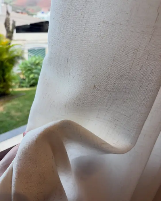 Close do tecido de linho natural de uma cortina, com o jardim ao fundo