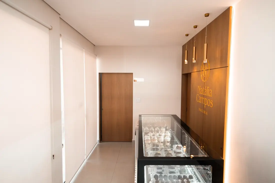 Salão comprido da doceria com vitrine e janelas com persianas rolô