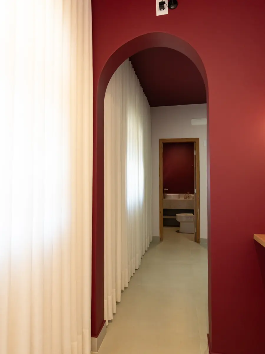Cortina de linho do chão ao teto ao lado de um arco bordô, com corredor claro ao fundo