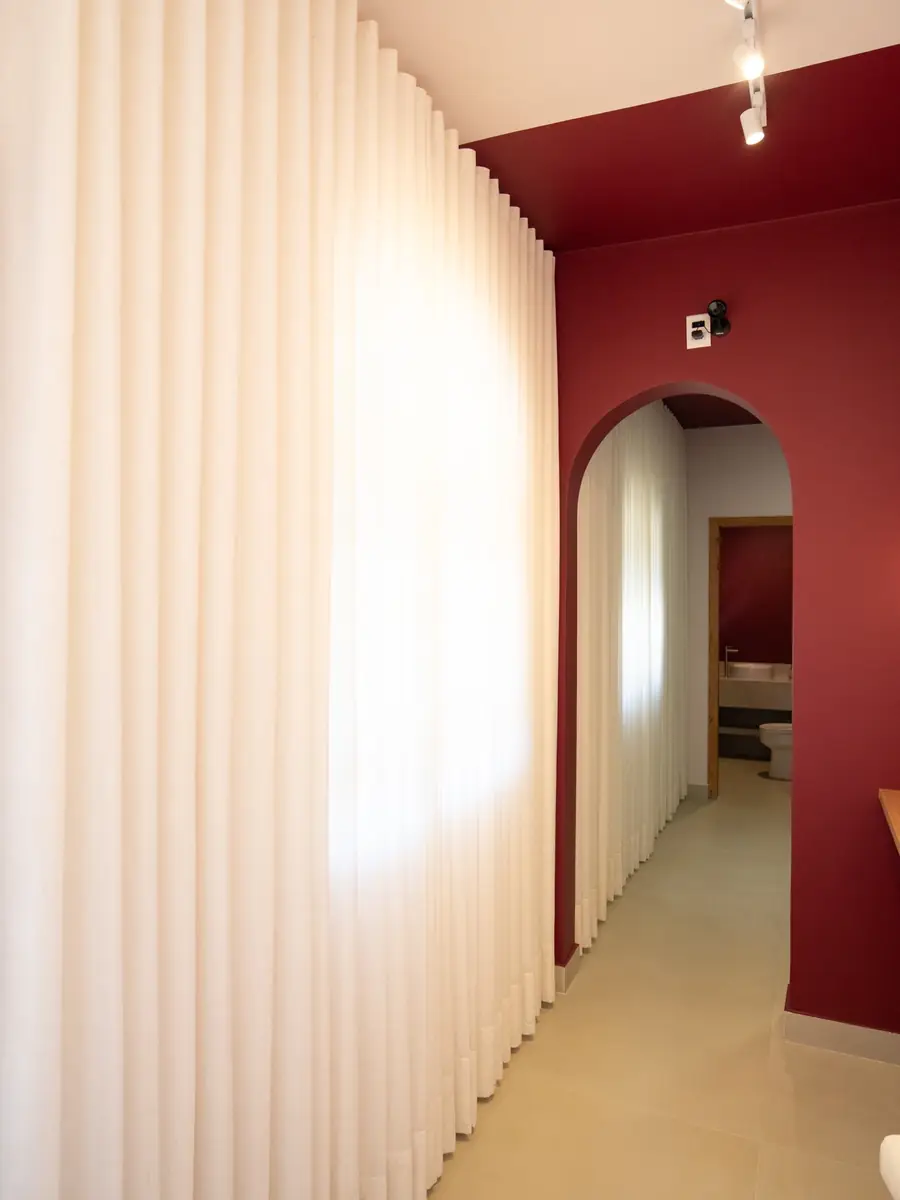 Cortina de linho e arco bordô emoldurando a passagem para o lavabo