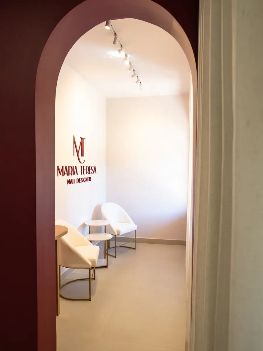 Entrada do studio vista pelo arco, com a marca Maria Teresa na parede e poltronas brancas