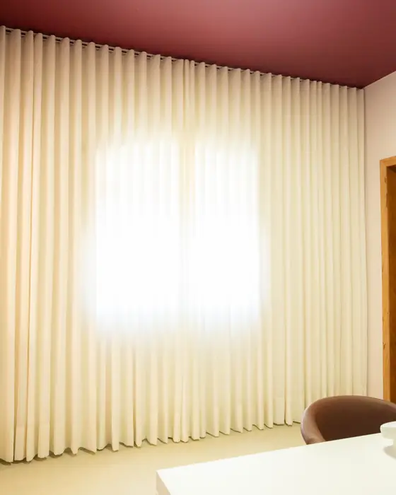 Parede inteira de cortina de linho natural em ondas, iluminada pela luz da janela